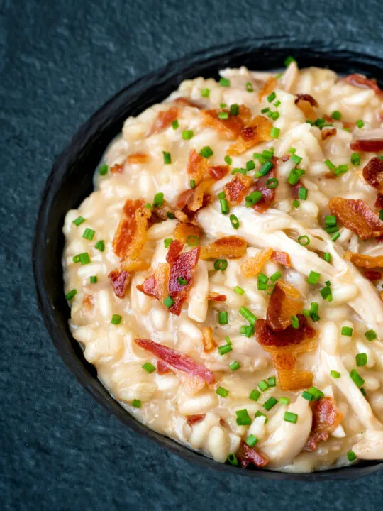 Close up creamy chicken and bacon risotto with snipped chives served in a black bowl.