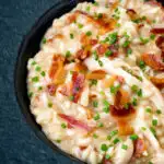 Close up creamy chicken and bacon risotto with snipped chives served in a black bowl featuring a title overlay.