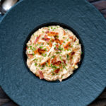 Overhead creamy chicken and bacon risotto with snipped chives served in a black bowl.