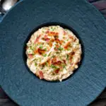 Overhead creamy chicken and bacon risotto with snipped chives served in a black bowl.