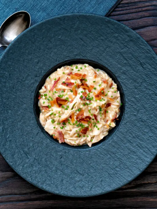 Overhead creamy chicken and bacon risotto with snipped chives served in a black bowl.