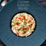 Overhead creamy chicken and bacon risotto with snipped chives served in a black bowl featuring a title overlay.