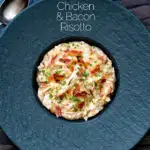 Overhead creamy chicken and bacon risotto with snipped chives served in a black bowl featuring a title overlay.
