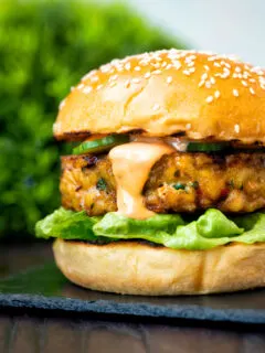Close up spicy cod fish burger with sriracha mayonnaise, lettuce and cucumber.