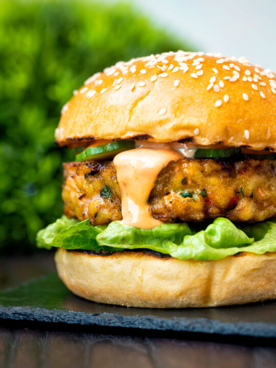 Close up spicy cod fish burger with sriracha mayonnaise, lettuce and cucumber.