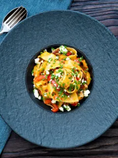 Overhead harissa pasta with with feta cheese and roasted peppers in a black bowl.