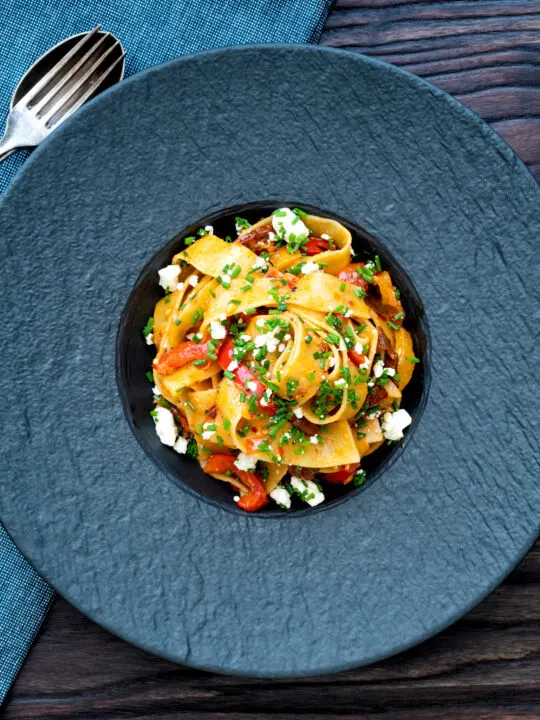 Overhead harissa pasta with with feta cheese and roasted peppers in a black bowl.