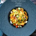 Overhead harissa pasta with with feta cheese and roasted peppers in a black bowl featuring a title overlay.