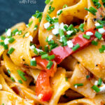 Close up harissa pasta with with feta cheese and roasted peppers in a black bowl featuring a title overlay.