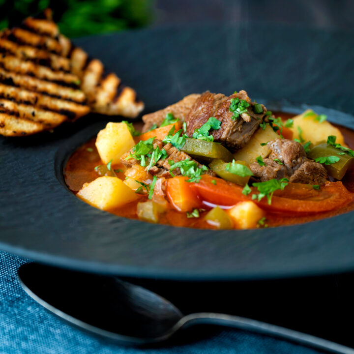 Hungarian lamb goulash soup served with griddled bread in a black bowl.