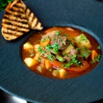 Hungarian lamb goulash garnished with parsley served in a black bowl.