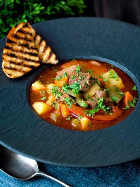 Hungarian lamb goulash garnished with parsley served in a black bowl.