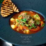 Hungarian lamb goulash garnished with parsley served in a black bowl featuring a title overlay.