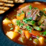 Close up Hungarian lamb goulash garnished with parsley served in a black bowl.