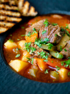 Close up Hungarian lamb goulash garnished with parsley served in a black bowl.