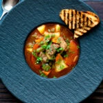 Overhead Hungarian lamb goulash garnished with parsley served in a black bowl.