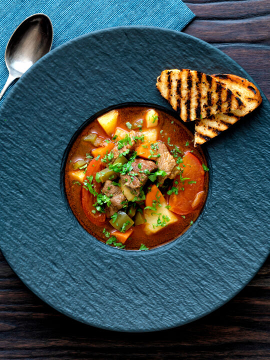 Overhead Hungarian lamb goulash garnished with parsley served in a black bowl.