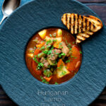 Overhead Hungarian lamb goulash garnished with parsley served in a black bowl featuring a title overlay.