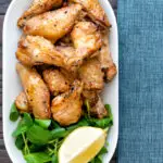 Overhead crispy lemon pepper chicken wings served with a green salad and lemon wedge.