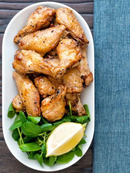 Overhead crispy lemon pepper chicken wings served with a green salad and lemon wedge.