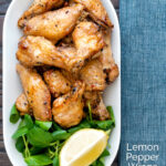 Overhead crispy lemon pepper chicken wings served with a green salad and lemon wedge featuring a title overlay.