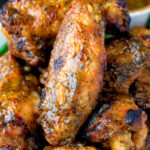 Close up spicy mango habanero hot wings served with extra dipping sauce.