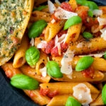 Close up Italian penne arrabbiata served with basil, parmesan, black pepper and cheesy garlic.