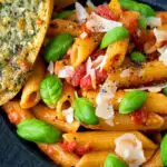 Close up Italian penne arrabbiata served with basil, parmesan, black pepper and cheesy garlic bread featuring a title overlay.