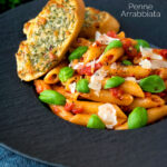 Italian penne arrabbiata served with basil, parmesan, black pepper and cheesy garlic bread featuring a title overlay.