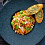 Overhead Italian penne arrabbiata served with basil, parmesan, black pepper and cheesy garlic bread.