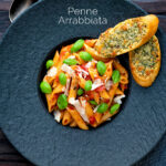 Overhead Italian penne arrabbiata served with basil, parmesan, black pepper and cheesy garlic bread featuring a title overlay.