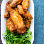 Overhead pineapple and jalapeno pepper glazed chicken wings served with rocket featuring a title overlay.