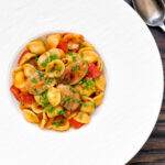 Overhead sausage and pepper orecchiette pasta in a light tomato sauce with fresh parsley.