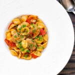 Overhead sausage and pepper orecchiette pasta in a light tomato sauce with fresh parsley.