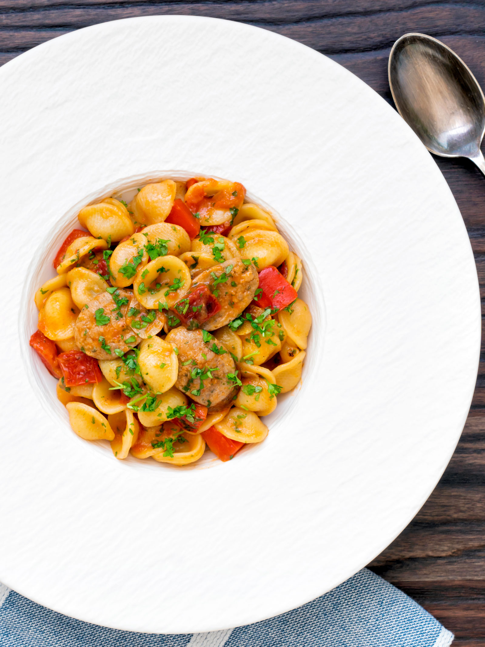 Overhead sausage and pepper orecchiette pasta in a light tomato sauce with fresh parsley.