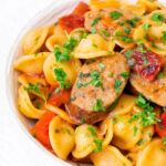 Close up sausage and pepper orecchiette pasta in a light tomato sauce with fresh parsley.