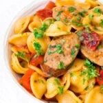 Close up sausage and pepper orecchiette pasta in a light tomato sauce with fresh parsley.