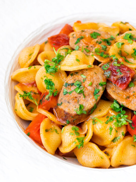 Close up sausage and pepper orecchiette pasta in a light tomato sauce with fresh parsley.
