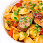 Close up sausage and pepper orecchiette pasta in a light tomato sauce with fresh parsley featuring a title overlay.