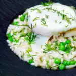 Close up smoked haddock risotto with peas topped with a poached egg and fresh dill.
