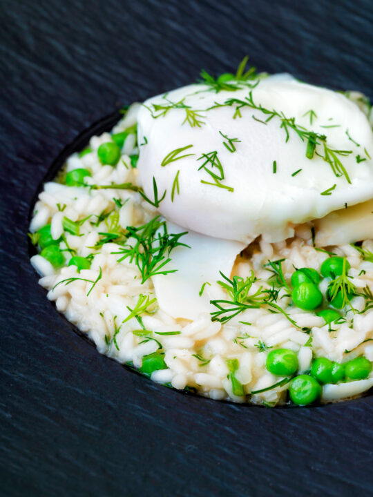 Close up smoked haddock risotto with peas topped with a poached egg and fresh dill.