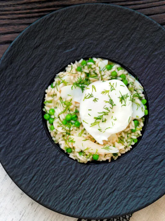 Overhead smoked haddock risotto with peas topped with a poached egg and fresh dill.