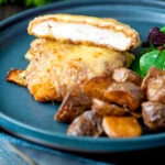 Cut open chicken parmo cheese topped breaded chicken escalope served with fried potatoes.