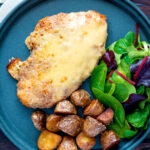 Overhead chicken parmo cheese topped breaded chicken escalope served with fried potatoes featuring a title overlay.