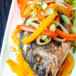 Close up Jamaican influenced escovitch fish with sea bream and "pickled" peppers and onions featuring a title overlay.