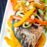 Close up Jamaican influenced escovitch fish with sea bream and "pickled" peppers and onions featuring a title overlay.