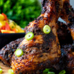 Close up Jamaican jerk chicken drumstick with green onions.