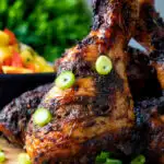 Close up Jamaican jerk chicken drumstick with green onions.