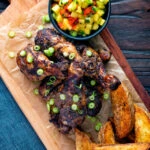 Overhead Jamaican jerk chicken drumsticks with potato wedges and mango salsa.