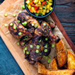 Overhead Jamaican jerk chicken drumsticks with potato wedges and mango salsa featuring a title overlay.